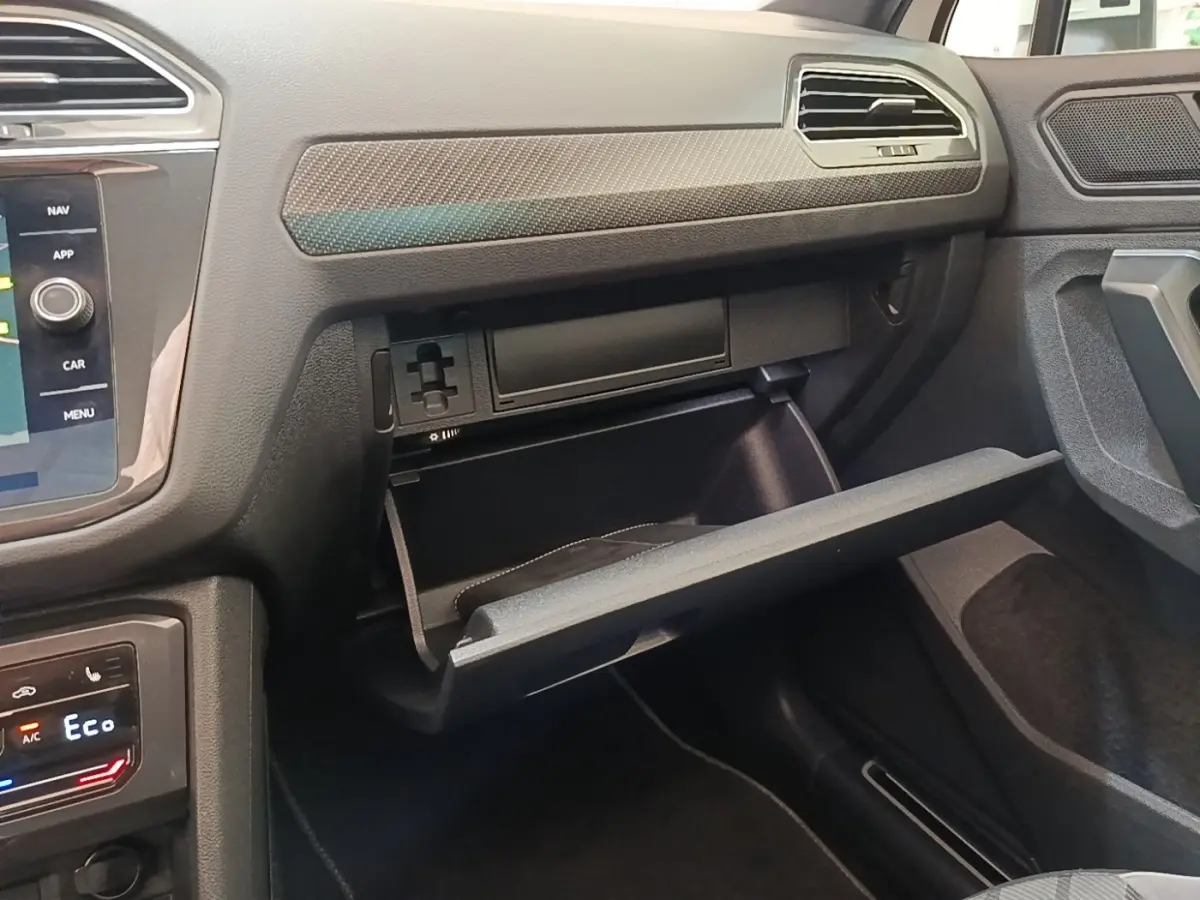 Intérieur Volkswagen Tiguan 2023 blanc, vue côté passager sur la boîte à gants ouverte et tableau de bord moderne.