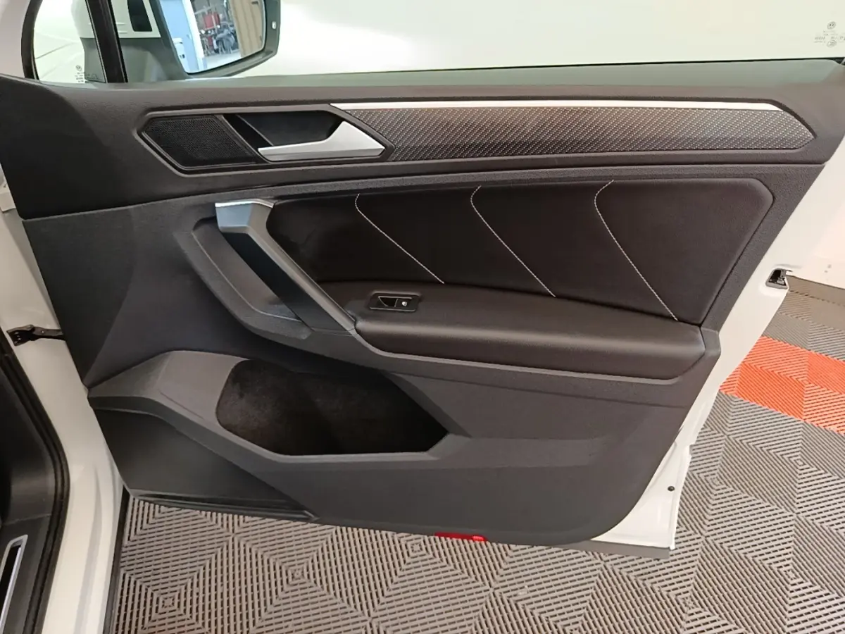 Vue intérieure de la porte avant gauche du Volkswagen Tiguan blanc, avec garniture noire et insert effet carbone.