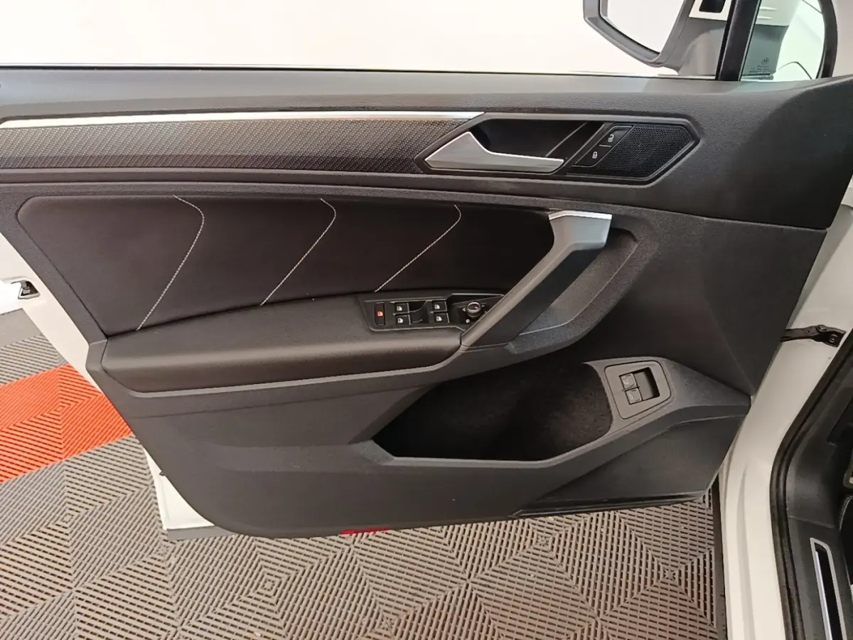 Vue intérieure côté gauche de la porte avant d’un Volkswagen Tiguan blanc avec garniture noire et commandes électriques.