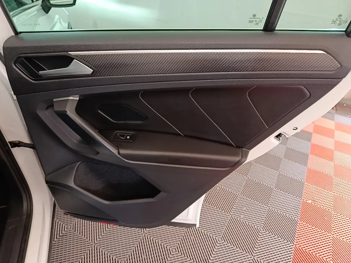 Vue intérieure de la porte arrière gauche du Volkswagen Tiguan blanc 2023 avec garniture noire et surpiqûres blanches.
