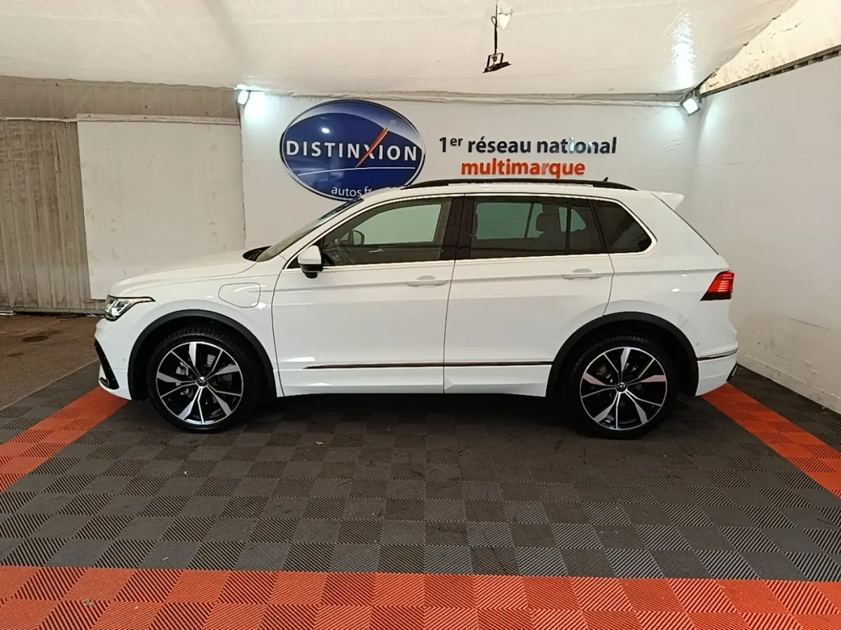 Vue de profil côté gauche d’un Volkswagen Tiguan blanc 2023 hybride rechargeable avec jantes alliage noires et toit ouvrant.