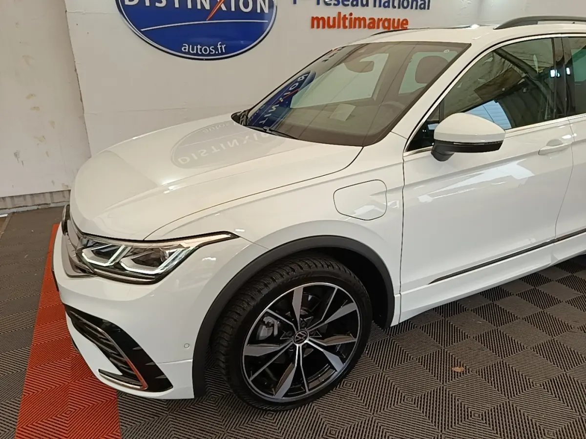 Vue 3/4 avant droit du Volkswagen Tiguan blanc hybride rechargeable avec jantes alliage noires et détails R-Line.