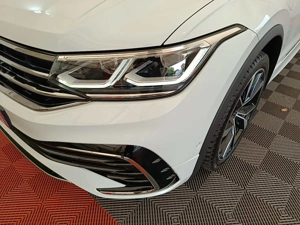 Gros plan sur l'avant droit blanc du Volkswagen Tiguan 1.4 eHybrid 2023, mettant en valeur le phare LED et la jante alliage.