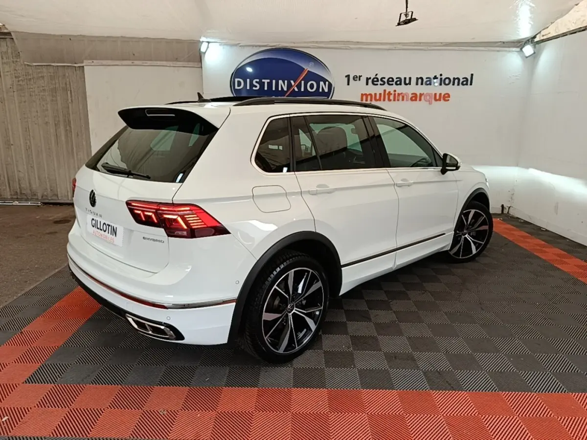 Volkswagen Tiguan blanc 1.4 eHybrid 245 DSG6 R-Line vu 3/4 arrière droit avec jantes noires et feux LED allumés.