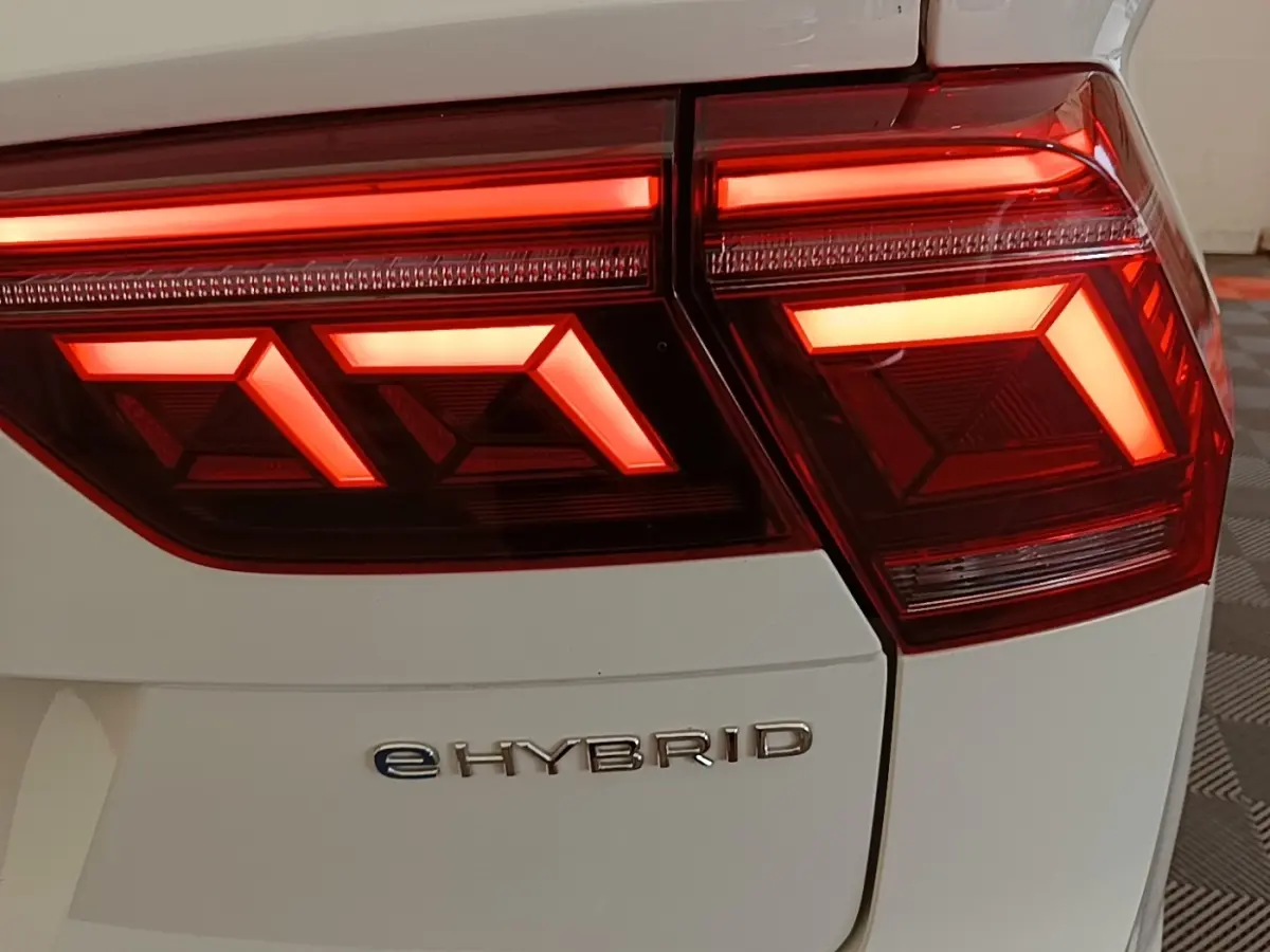 Gros plan sur le feu arrière droit rouge allumé du Volkswagen Tiguan blanc avec logo eHYBRID visible.