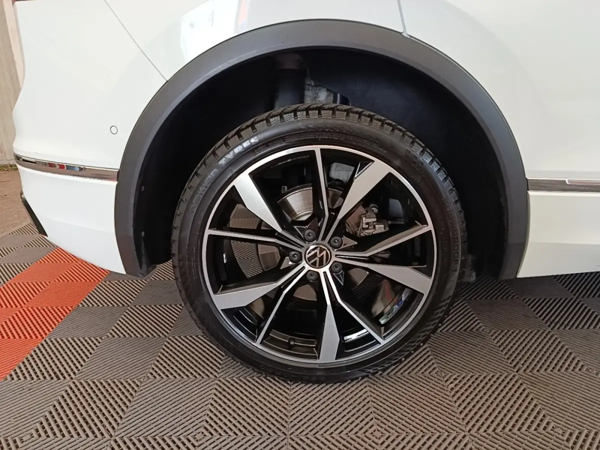 Gros plan sur la roue arrière droite du Volkswagen Tiguan blanc 2023 avec jante alliage noir et argentée R-Line.