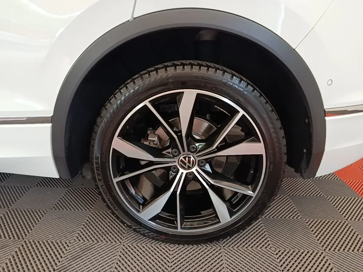 Gros plan sur la roue avant droite noire et argentée du Volkswagen Tiguan blanc 1.4 eHybrid 2023 R-Line.