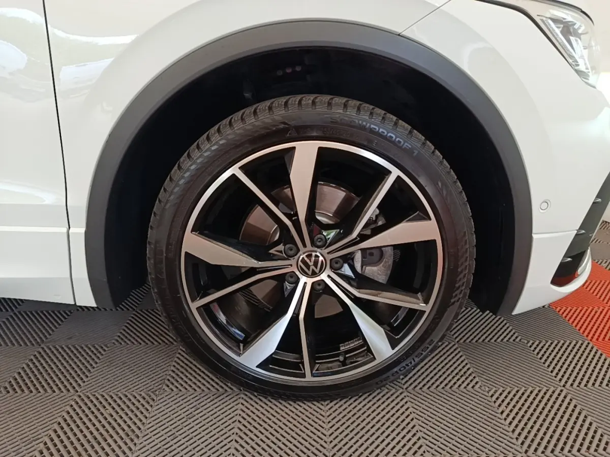 Gros plan sur la roue avant gauche du Volkswagen Tiguan blanc 2023 avec jante alliage R-Line noire et argentée.