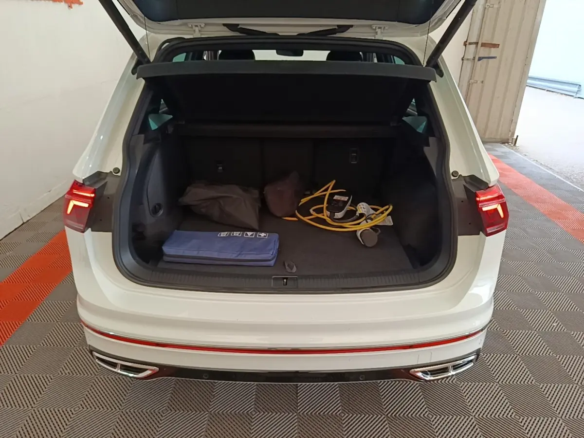 Vue arrière du coffre ouvert d’un Volkswagen Tiguan blanc 1.4 eHybrid 2023 avec câbles de recharge visibles.