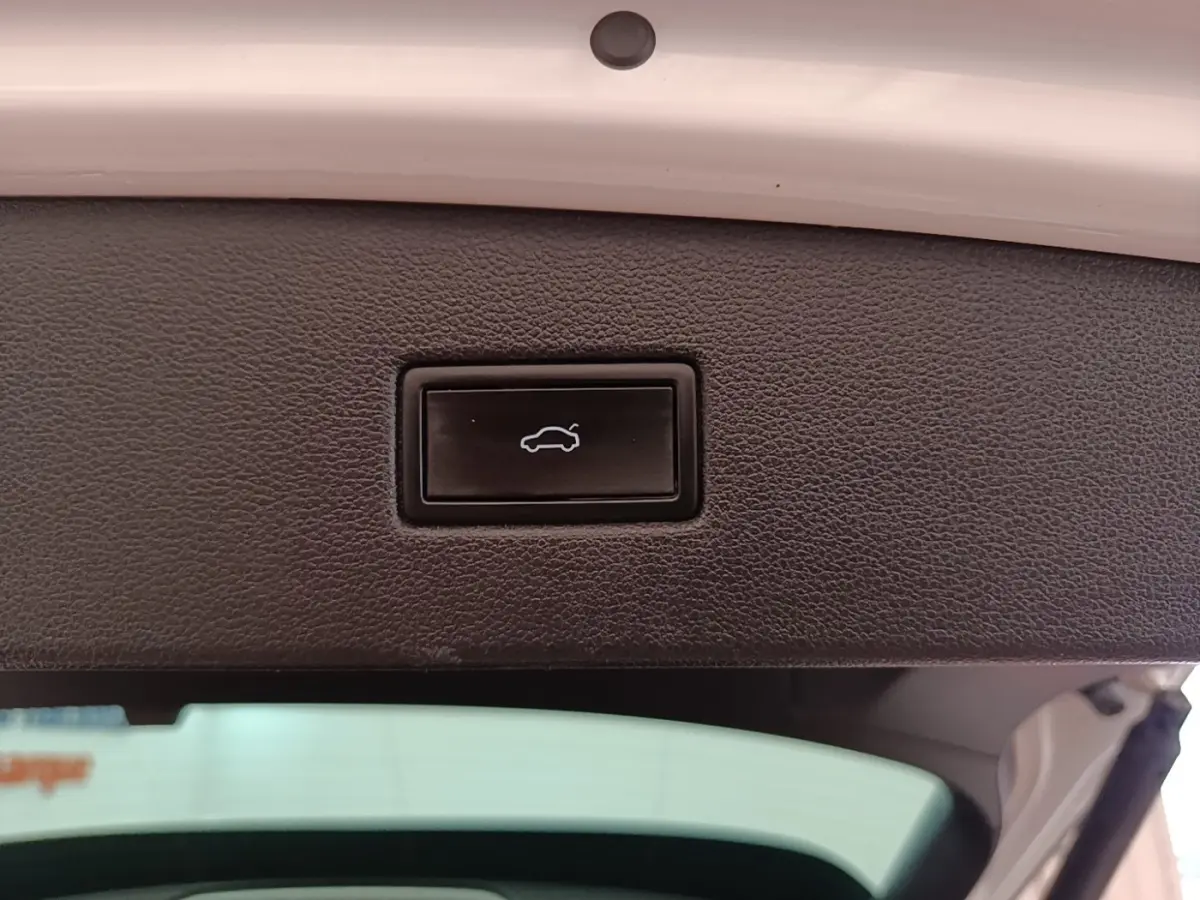 Gros plan sur le bouton d'ouverture électrique du coffre, intérieur du hayon blanc du Volkswagen Tiguan hybride 2023.