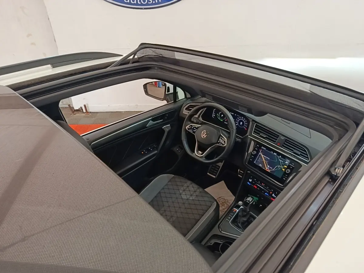 Vue intérieure par le toit ouvrant du Volkswagen Tiguan blanc, mettant en valeur le tableau de bord digital et le volant multifonctions.