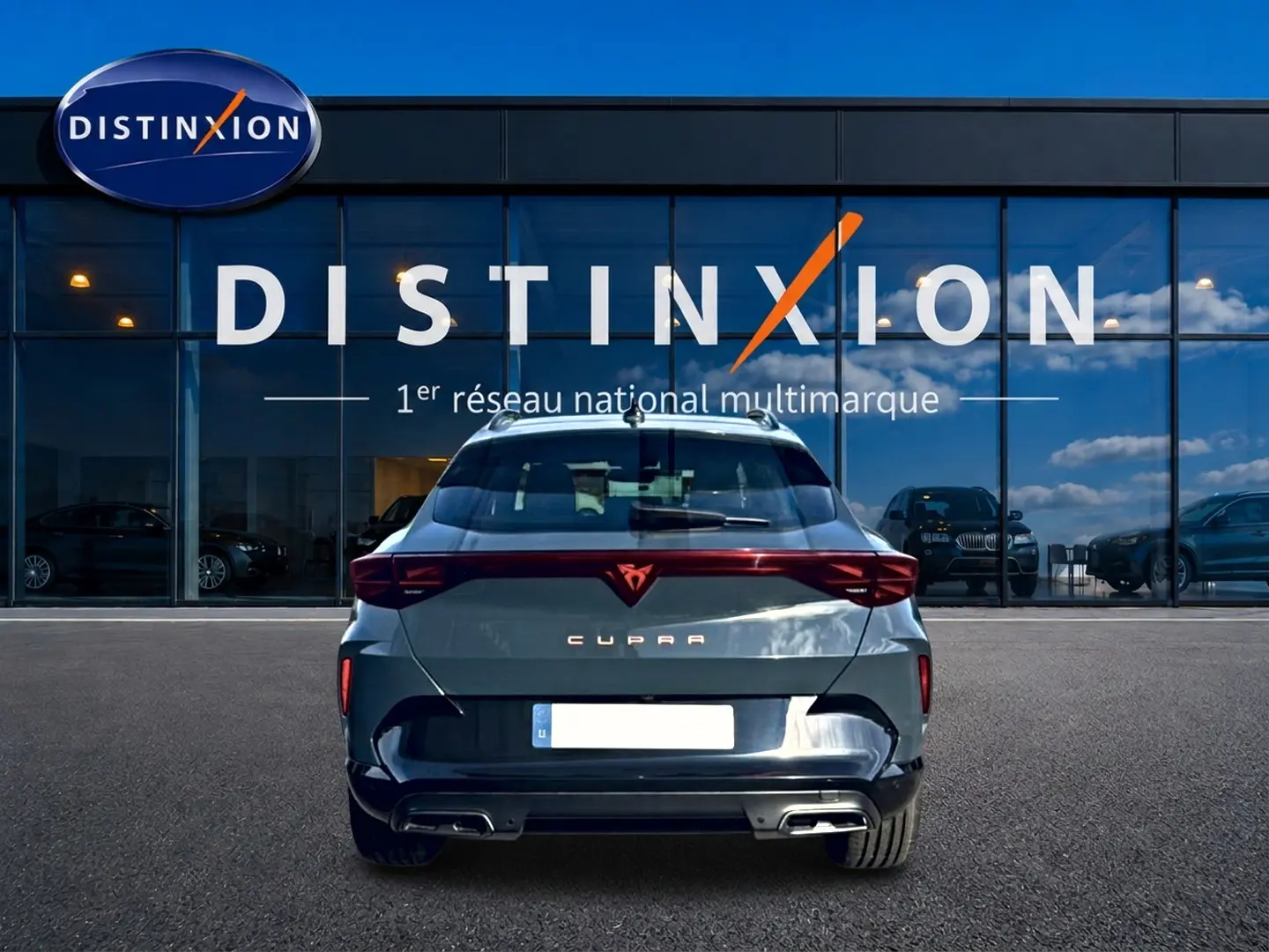 Vue arrière d'une CUPRA Formentor bleu fjord 2026 avec feux LED et double sortie d'échappement, stationnée devant un showroom.