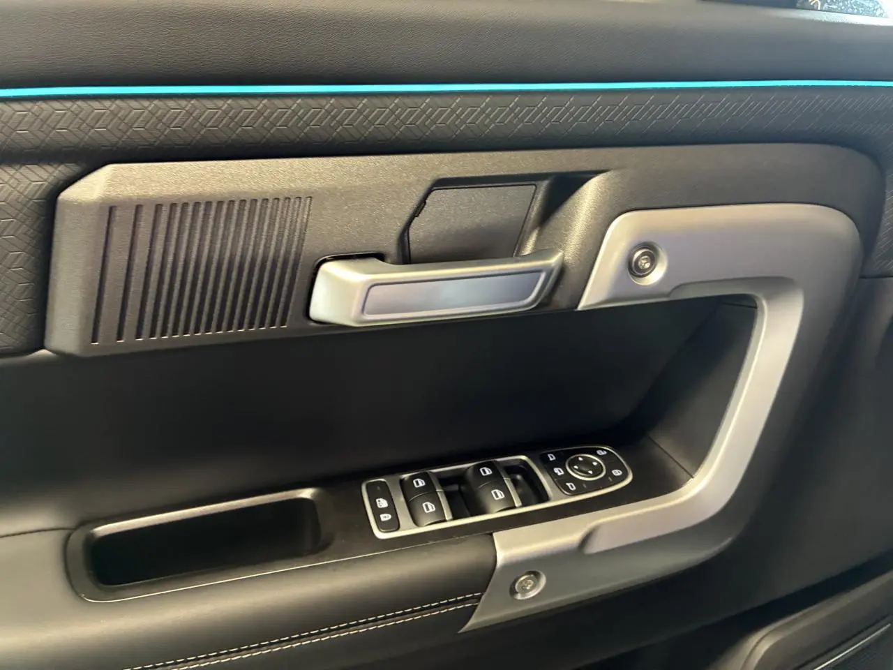 Gros plan sur la porte intérieure côté conducteur du JAECOO J7 gris olive, avec commandes électriques et poignée argentée.