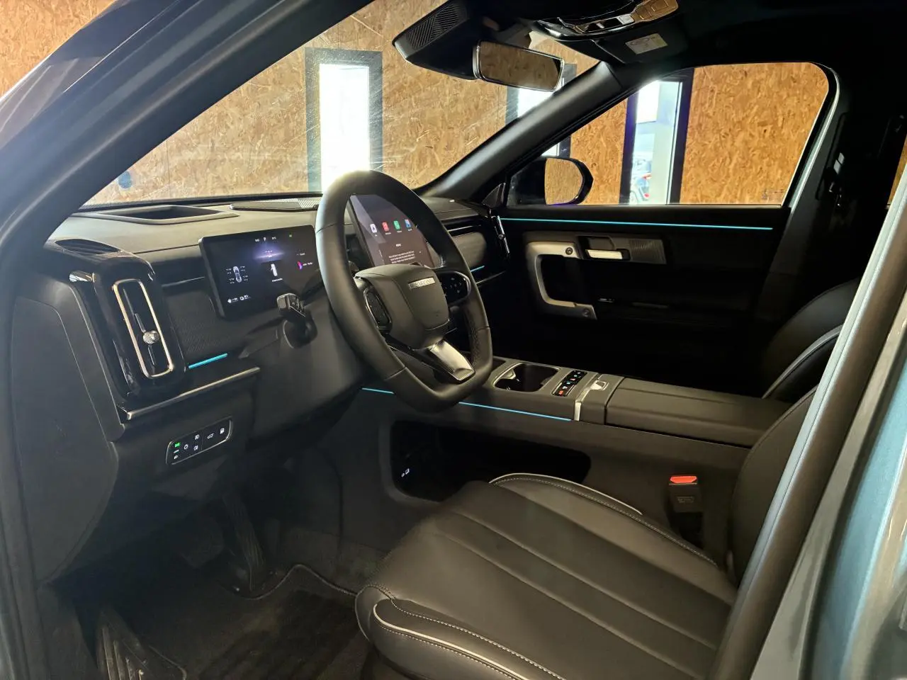 Vue intérieure côté conducteur du JAECOO J7 2026, sellerie cuir noir avec éclairage d'ambiance bleu subtil.