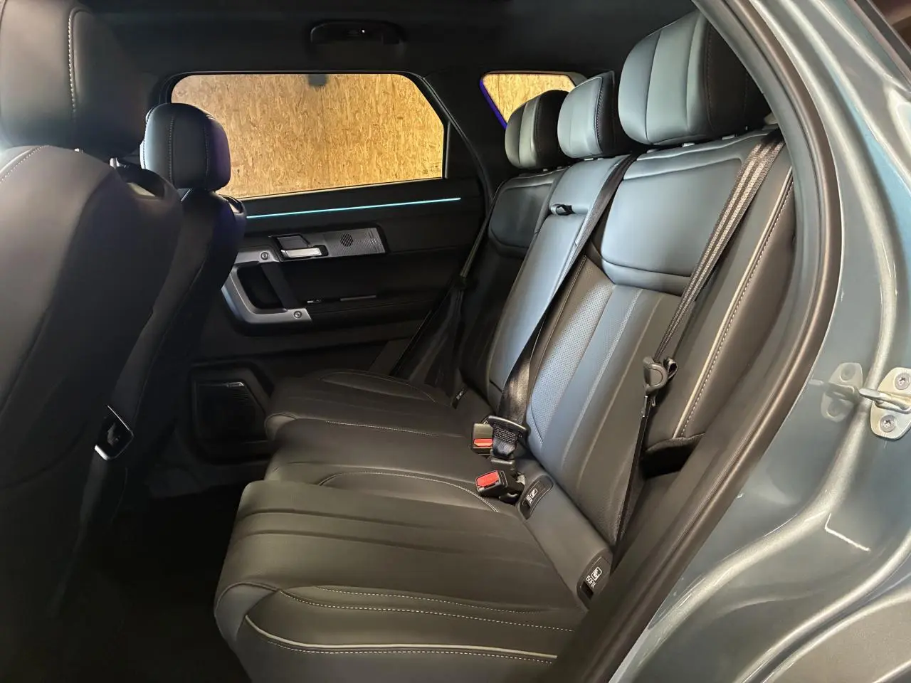 Vue intérieure côté droit sur les sièges arrière en cuir noir du JAECOO J7 2026 avec porte ouverte et éclairage d'ambiance bleu.