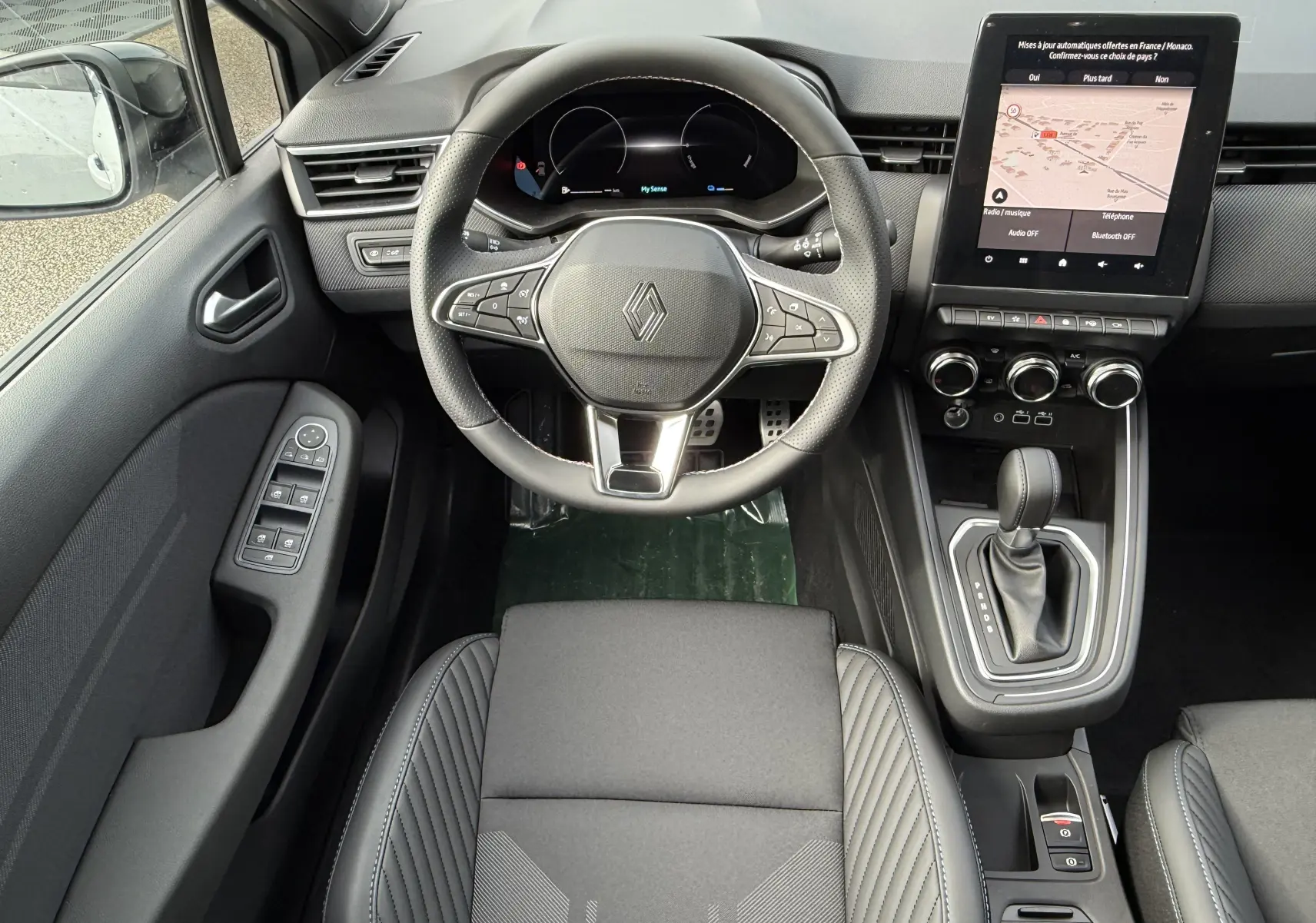 Vue intérieure de face du poste de conduite de la Renault Clio V hybride avec volant multifonction et écran tactile central.