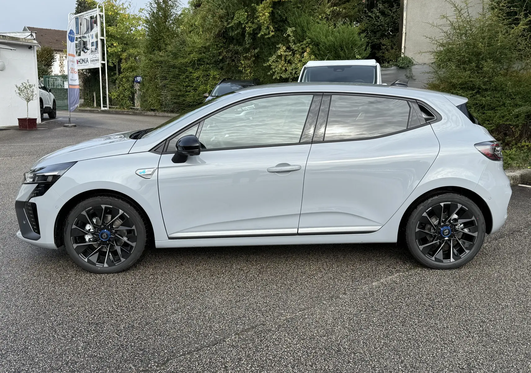 Profil côté gauche d'une Renault Clio V gris Rafale 2025 avec jantes noires et badges hybrides visibles.