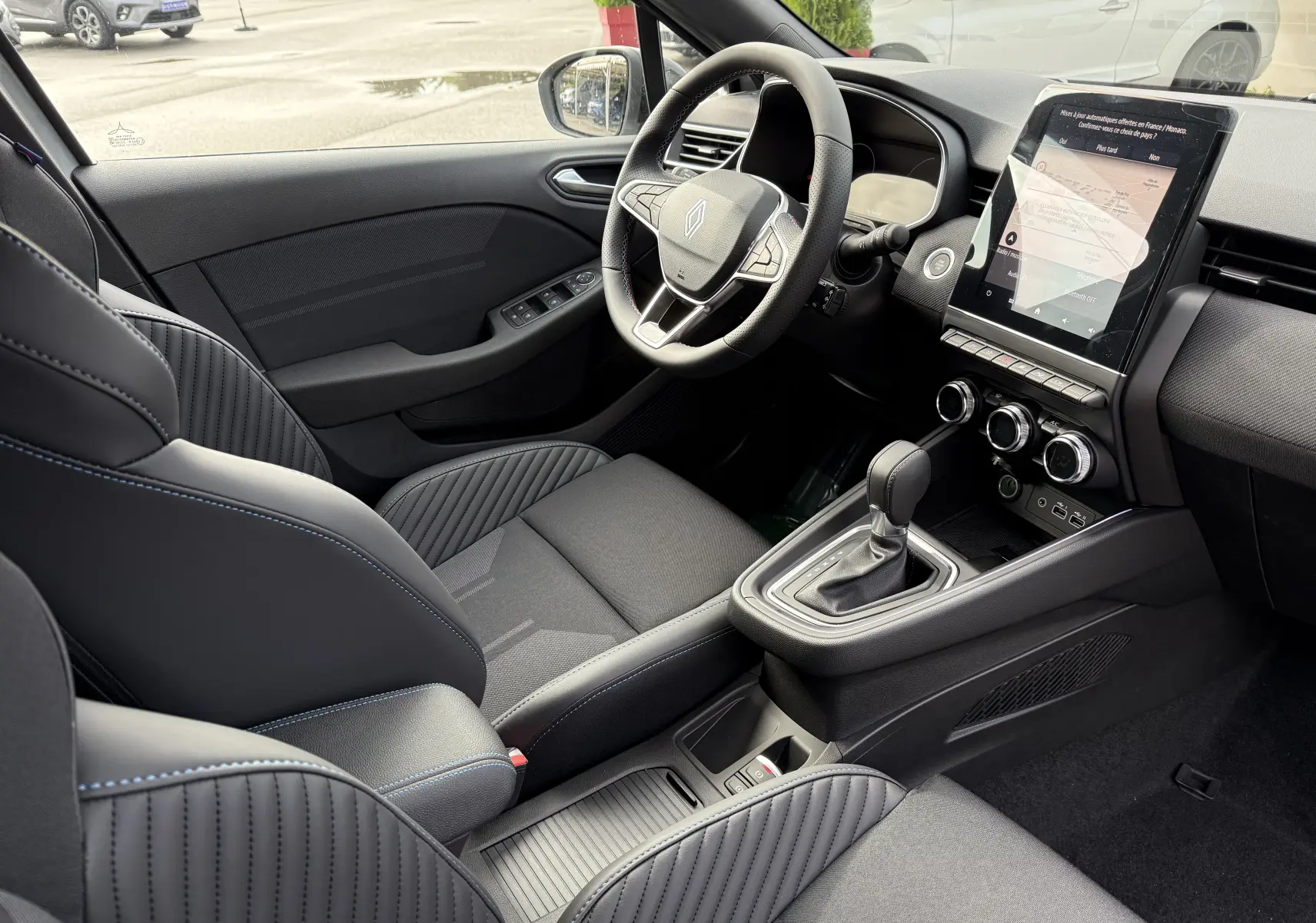 Intérieur de la Renault Clio V 1.6 E-TECH gris Rafale, vue côté conducteur, volant multifonction et écran tactile vertical.