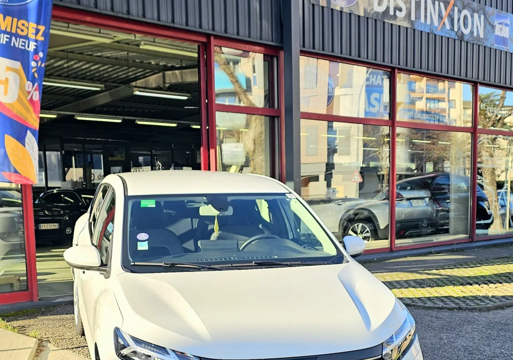 Vue 3/4 avant d'une Dacia Sandero III blanche glacier garée devant un garage avec logo AD Expert visible.