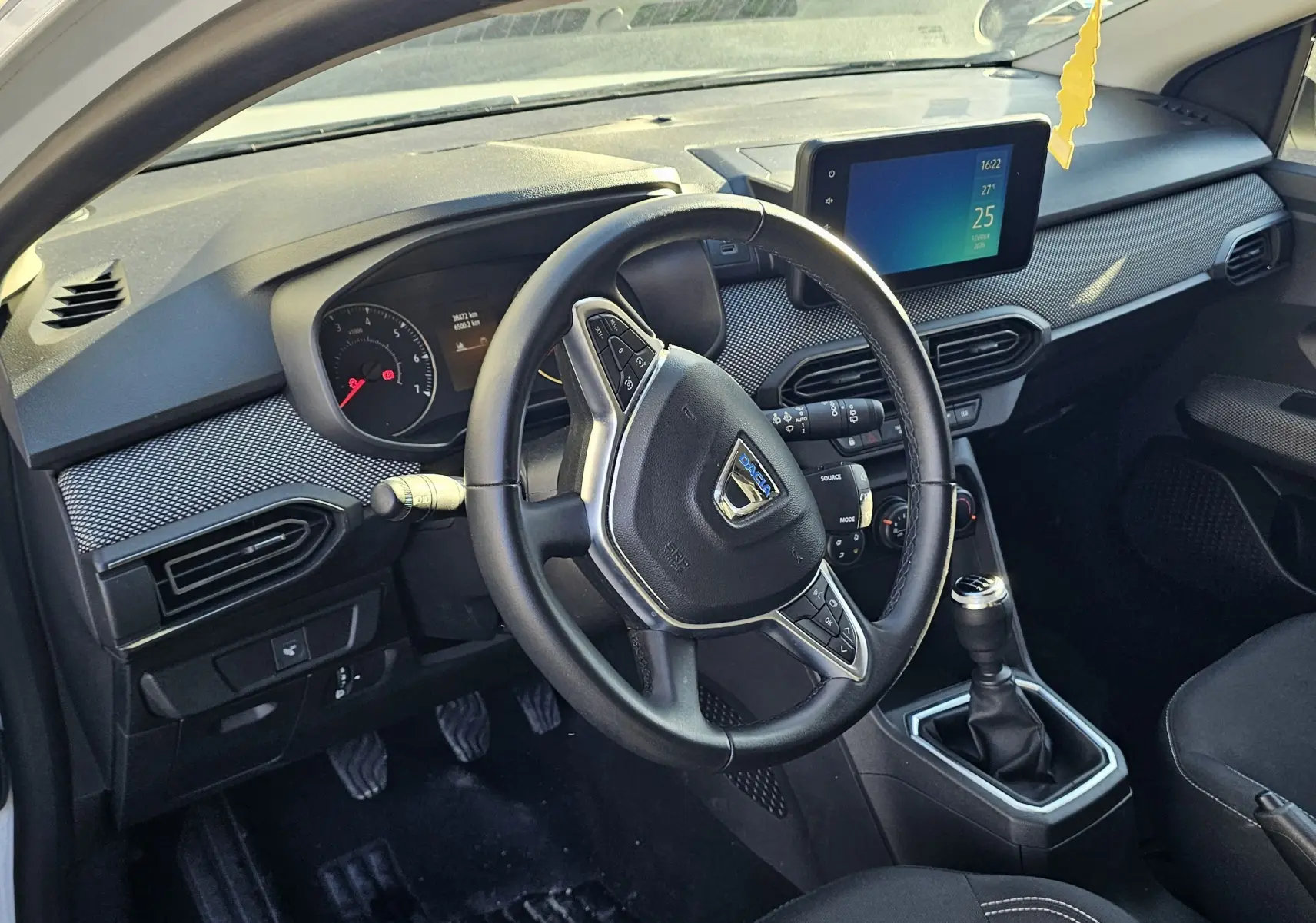 Vue intérieure côté conducteur de la Dacia Sandero III blanche, avec volant cuir multifonction et écran tactile central.