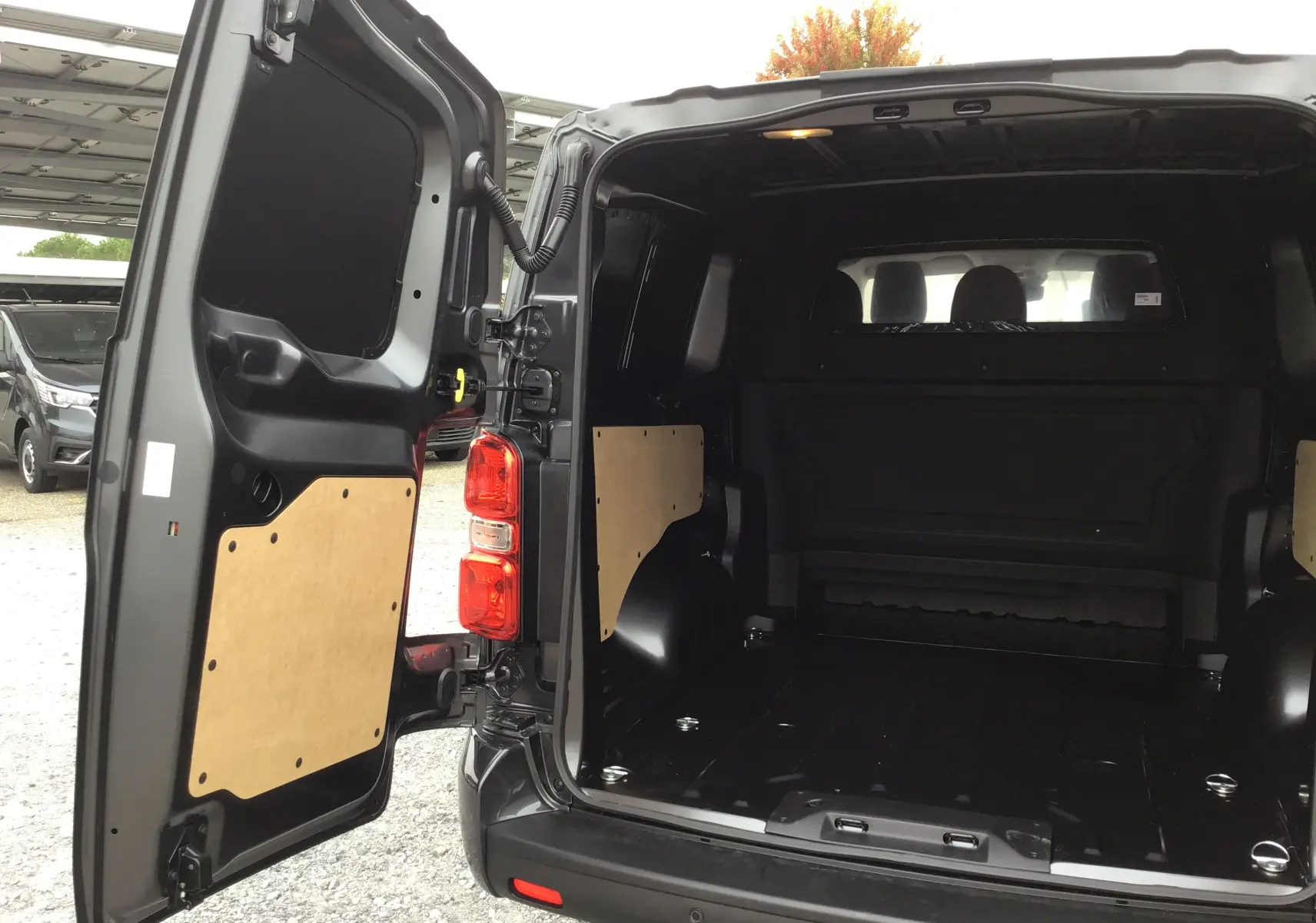Vue arrière ouverte du Peugeot Expert XL gris titane montrant l'espace de chargement vide avec protections en bois sur les portes.