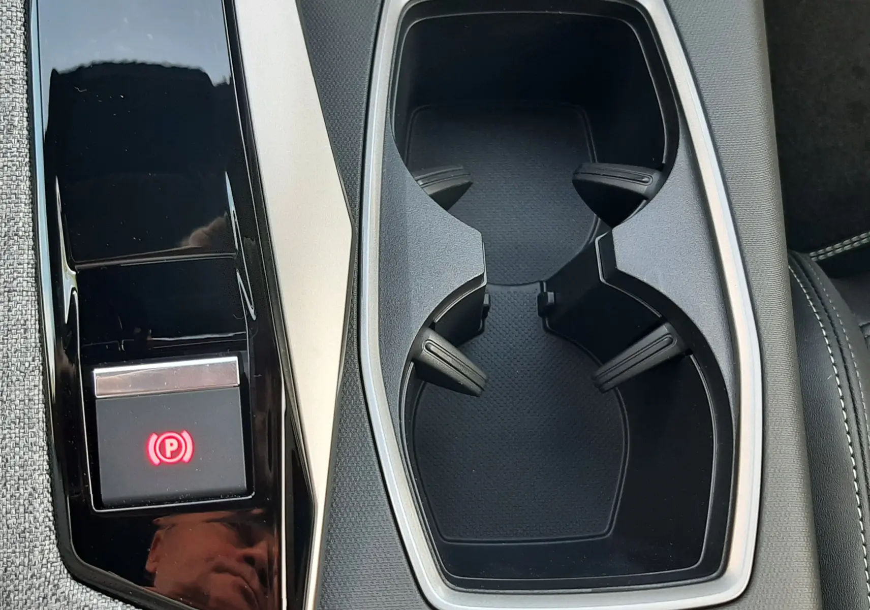 Gros plan sur la console centrale du Peugeot 3008 1.2 Hybrid GT 2026, avec porte-gobelets et frein à main électrique.