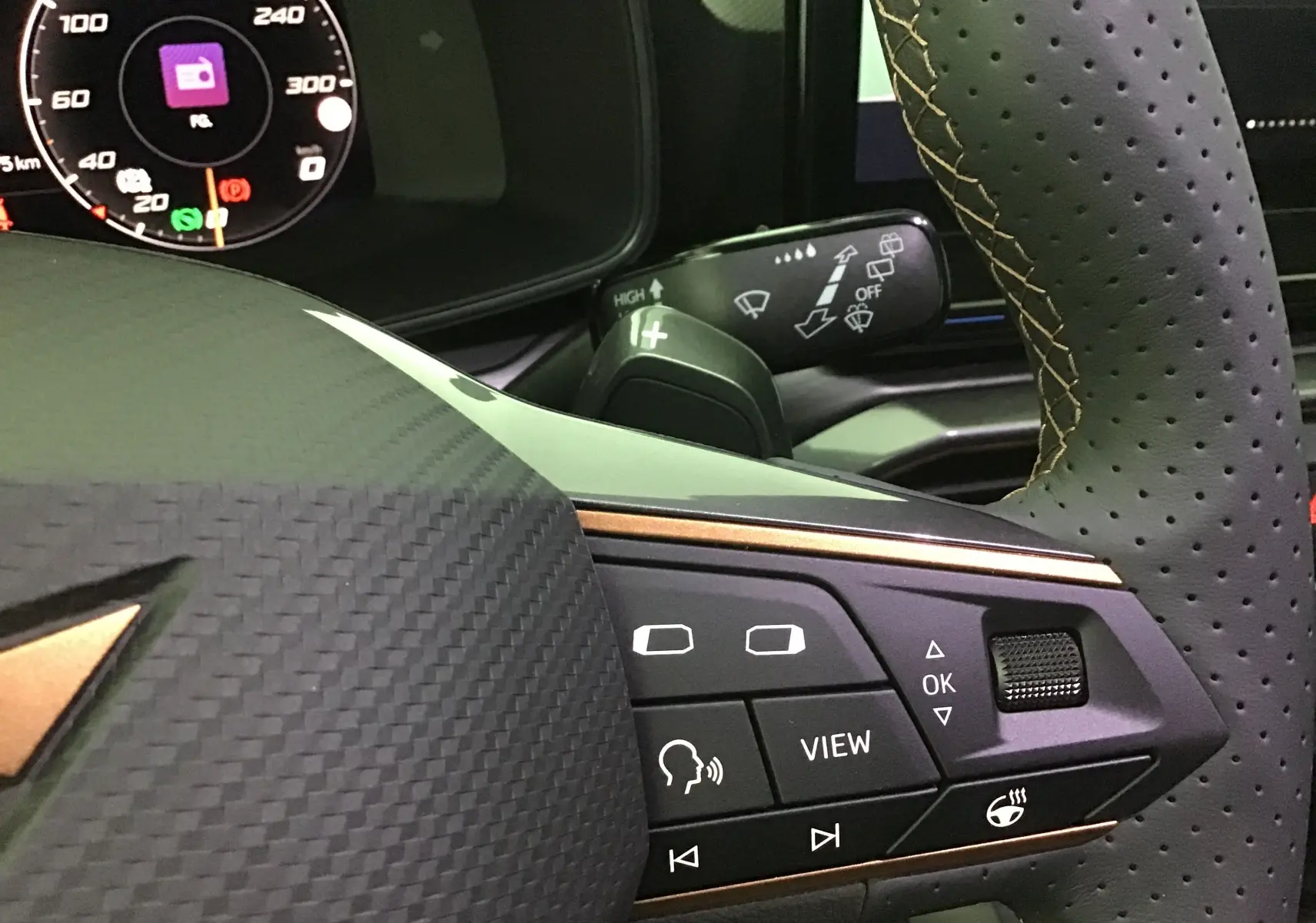 Gros plan sur le volant noir perforé avec surpiqûres cuivrées et commandes multifonctions du tableau de bord digital d'une CUPRA Leon 2023.