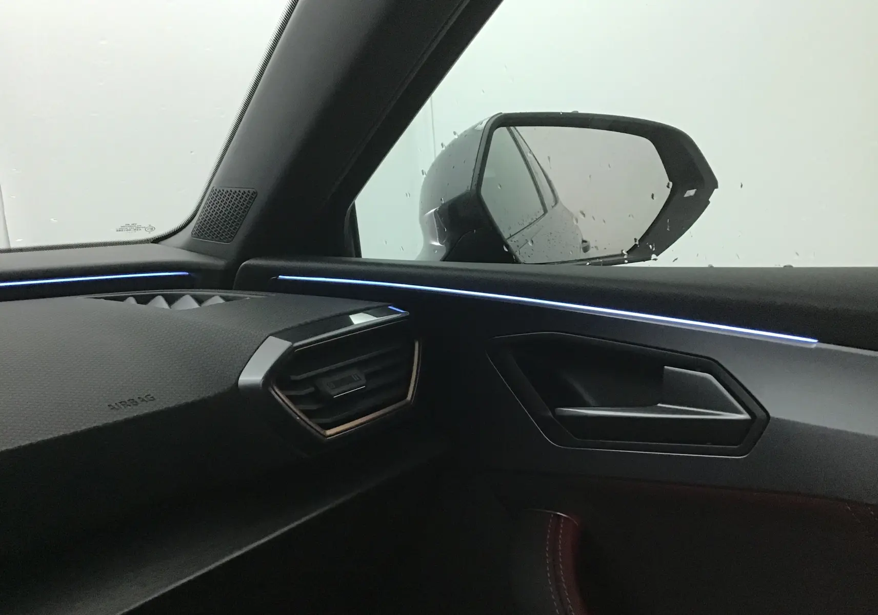 Vue intérieure côté passager du CUPRA Leon noir 2023, mettant en valeur la finition moderne avec éclairage d'ambiance bleu.