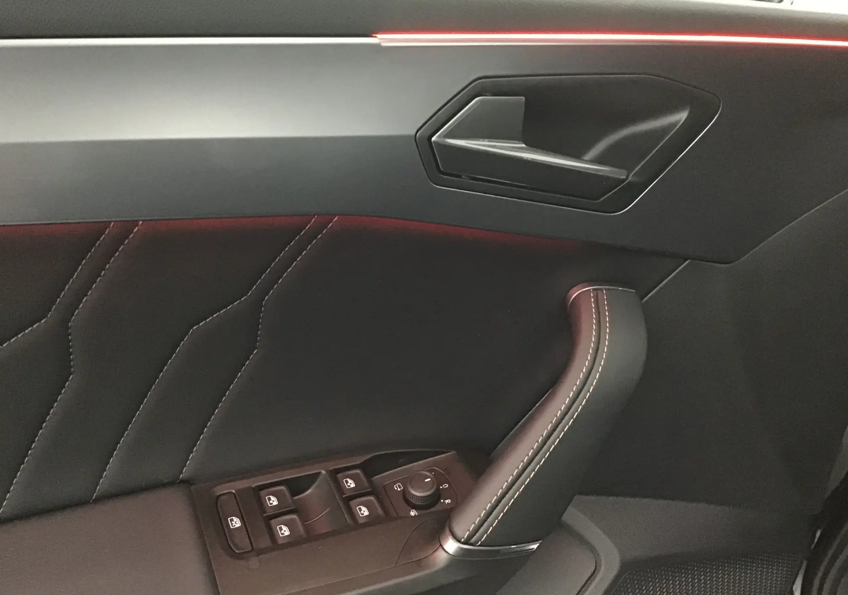 Détail de la porte côté conducteur de la CUPRA Leon 2023 noire, avec commandes des vitres et poignée en cuir surpiqué.