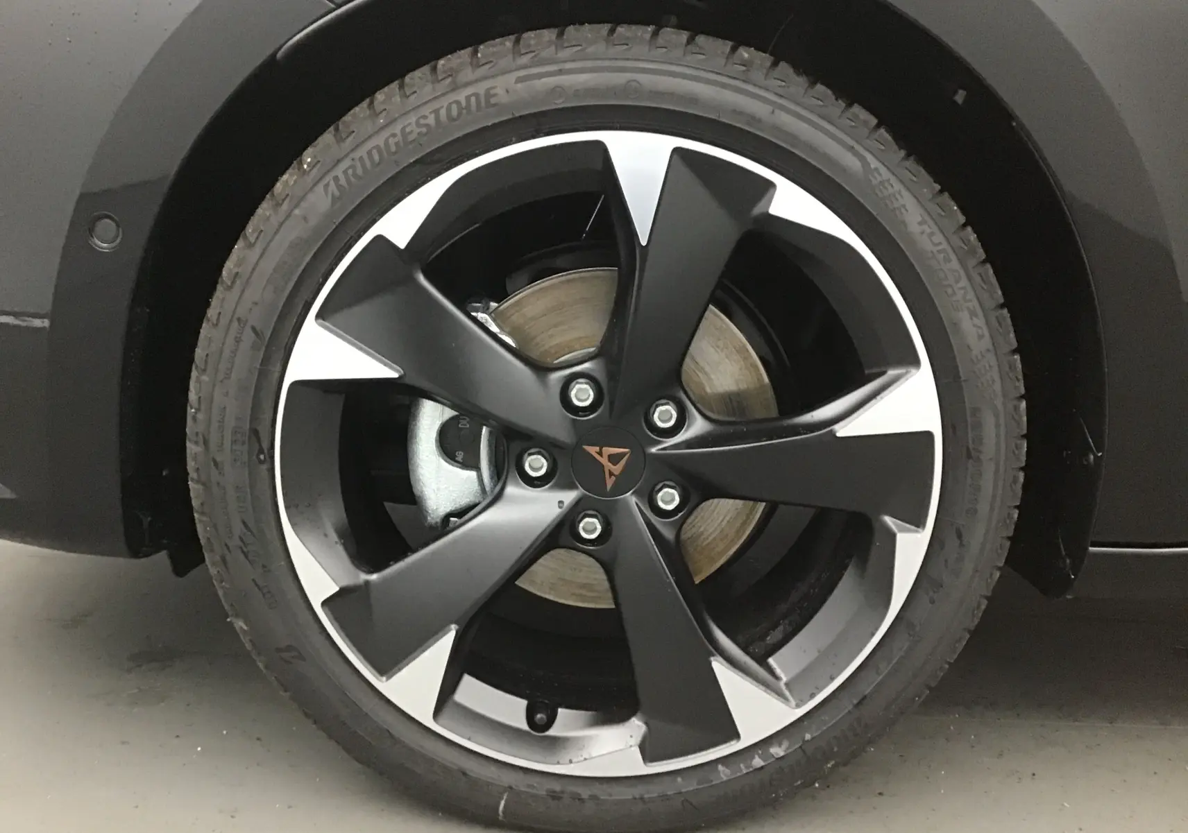 Gros plan sur la jante bi-ton noir et argent avec logo CUPRA sur une roue avant d'une CUPRA Leon noire 2023.