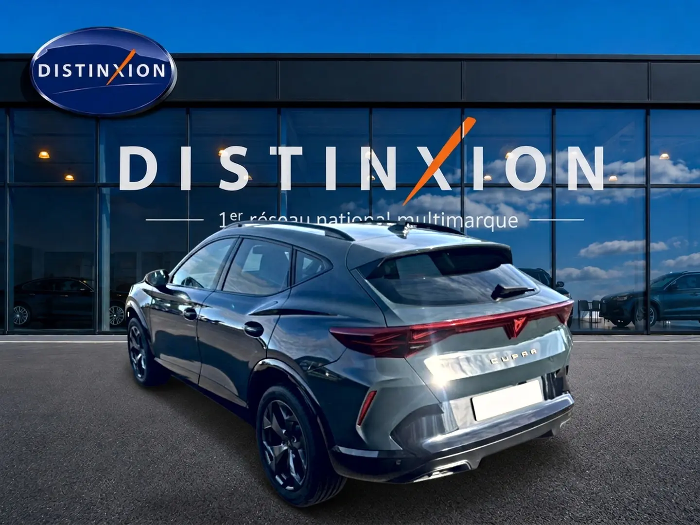 Vue 3/4 arrière droite d’un CUPRA Formentor bleu fjord 2026 avec feux arrière LED et jantes noires devant un showroom Distinxion.