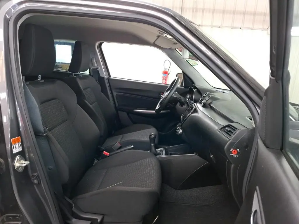 Vue intérieure côté conducteur de la Suzuki Swift grise 2023, montrant les sièges avant et le tableau de bord noir.