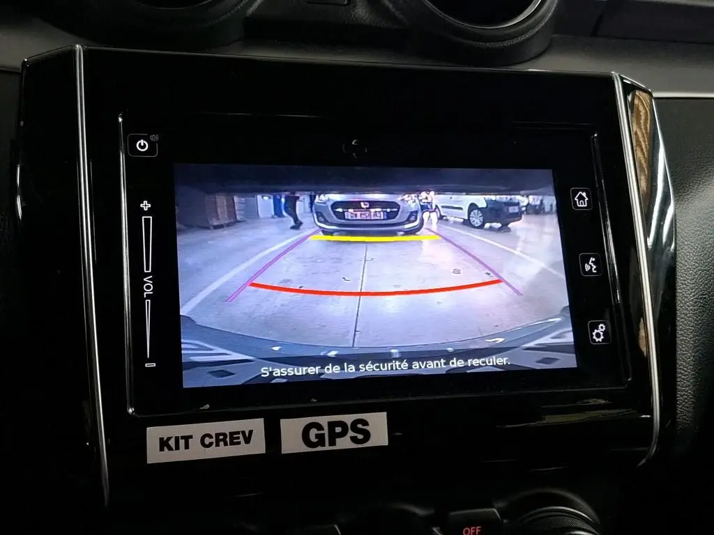 Écran central montrant la caméra de recul d’une Suzuki Swift grise 2023 avec guidage coloré en parking intérieur.