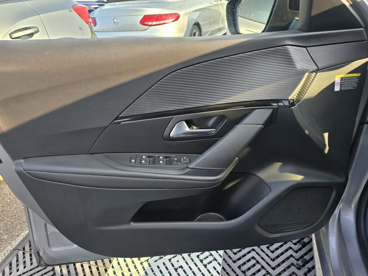 Vue intérieure côté gauche de la porte avant grise du Peugeot 208 II 1.2 GT PACK avec habillage carbone et commandes électriques.