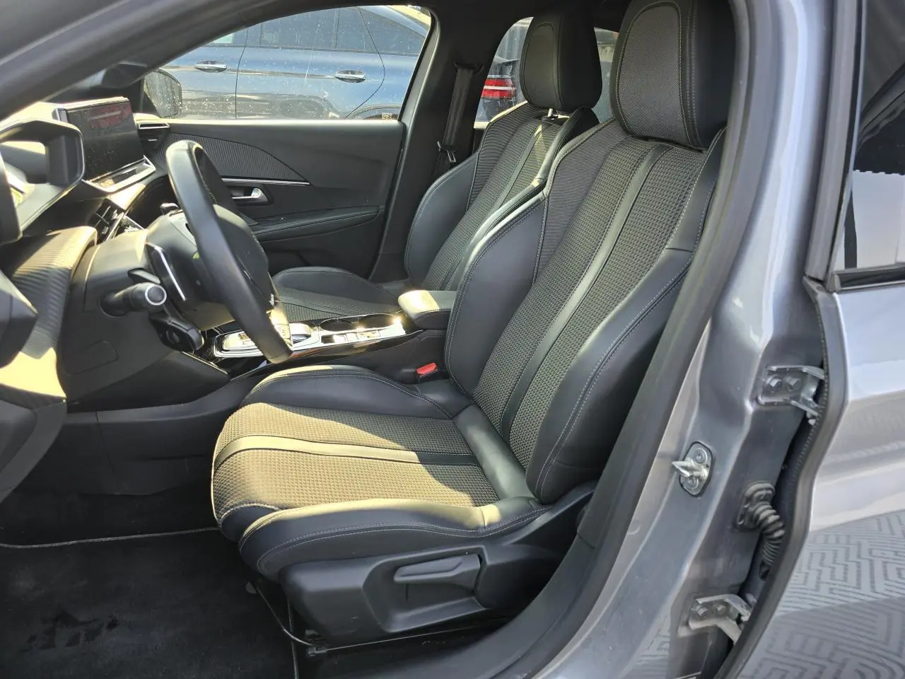 Vue intérieure côté conducteur de la Peugeot 208 grise 2023, sièges avant en tissu et TEP avec surpiqûres contrastées.