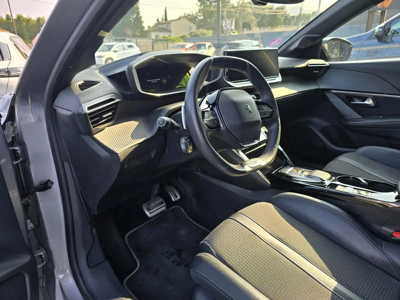 Vue intérieure côté conducteur de la Peugeot 208 grise 2023, avec volant compact et tableau de bord numérique.