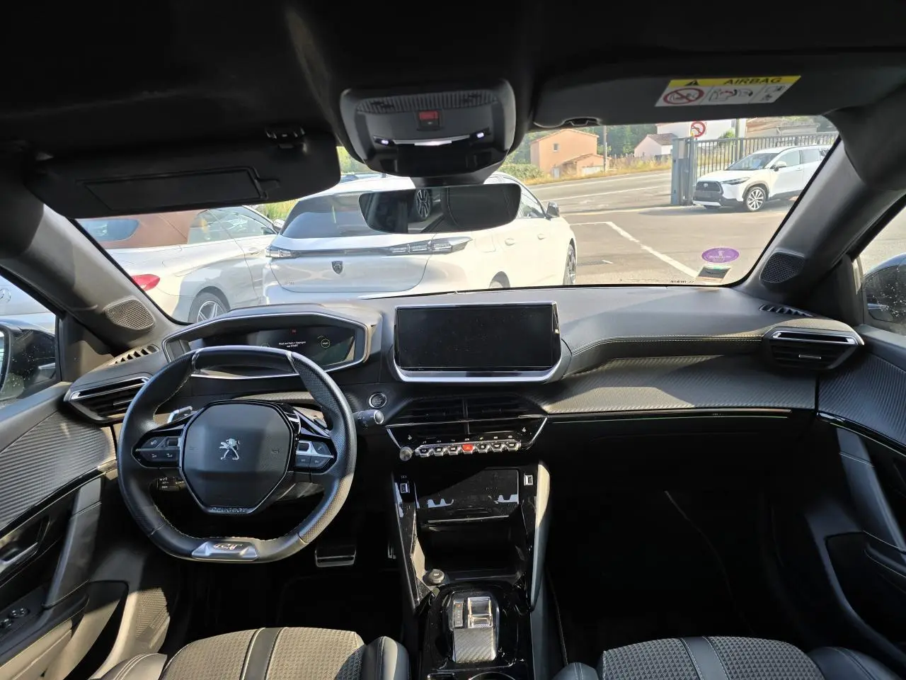 Vue intérieure avant du Peugeot 208 gris 2023, mettant en valeur le volant compact, l'écran tactile central et la planche de bord noire.