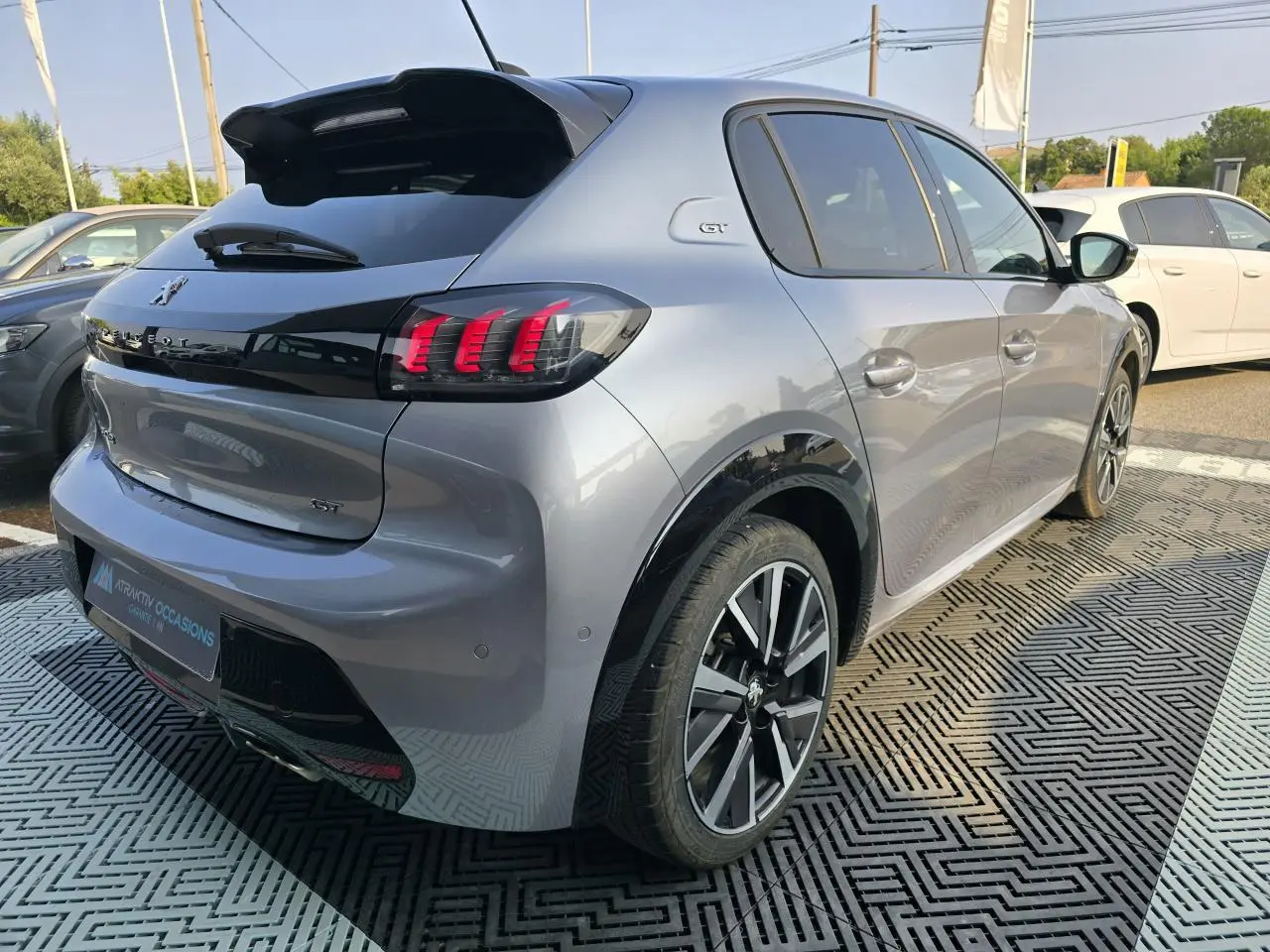 Vue 3/4 arrière droite d'une Peugeot 208 grise 2023 avec toit noir, feux arrière LED et jantes alliage 17 pouces.