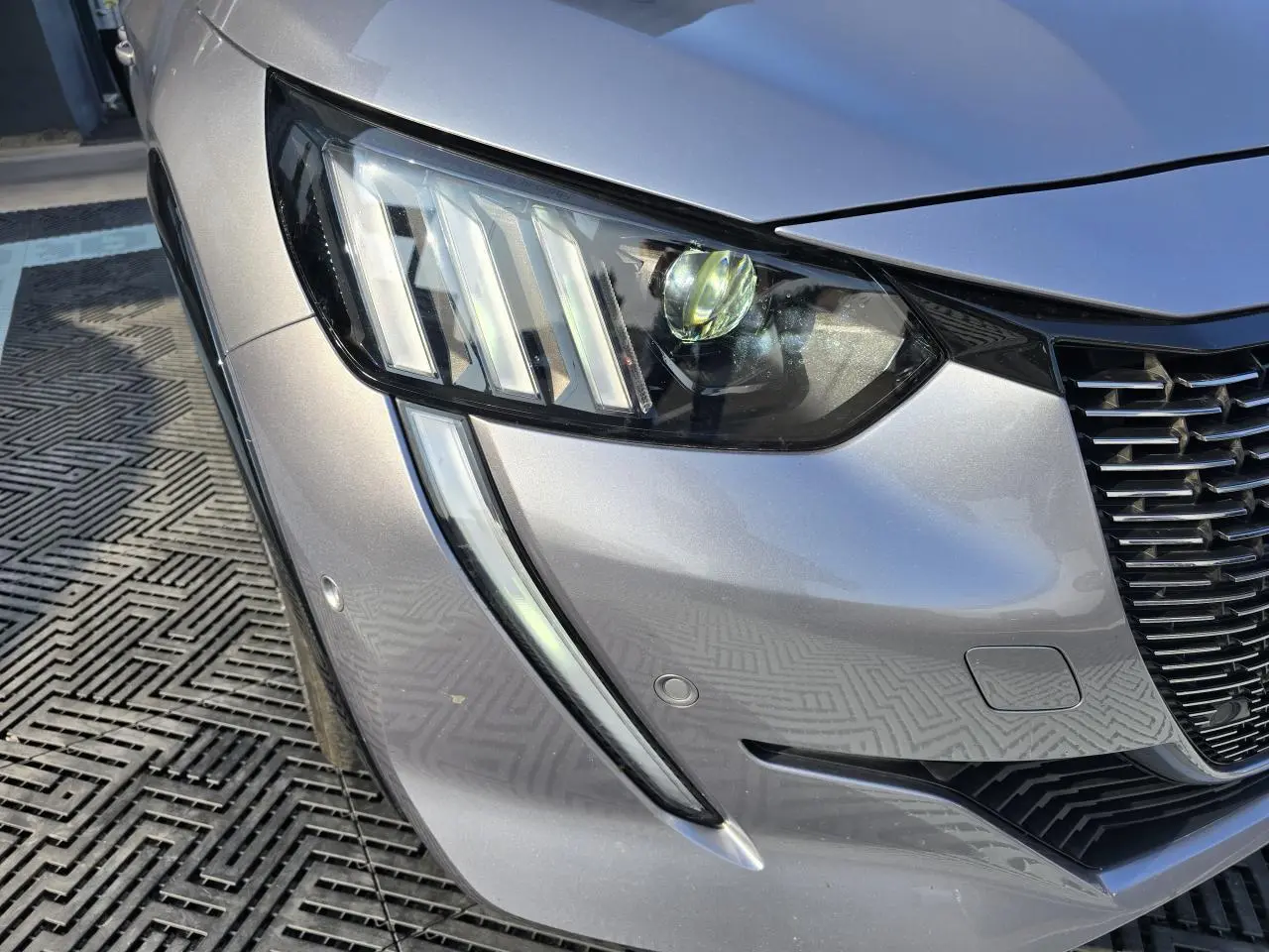 Gros plan sur le phare avant droit gris métallisé de la Peugeot 208 avec sa signature lumineuse verticale distinctive.