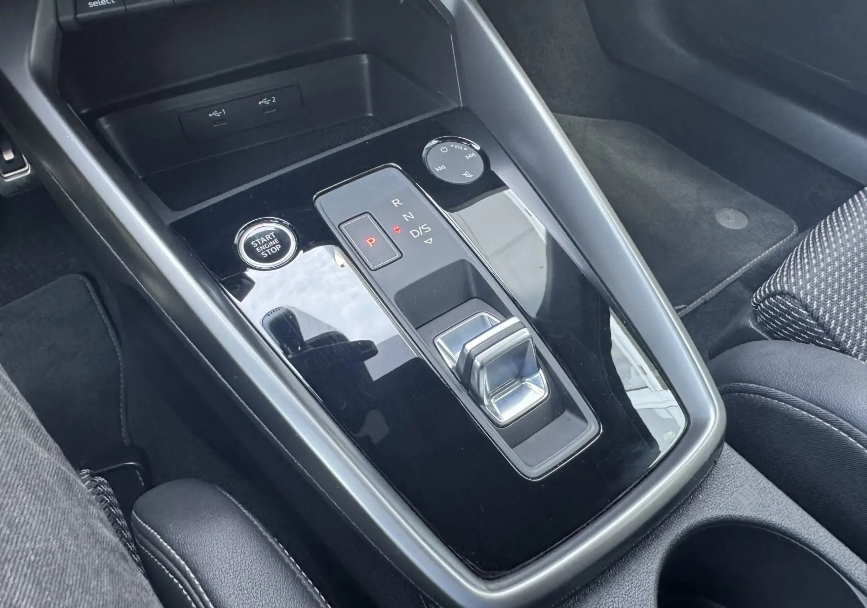 Vue rapprochée de la console centrale noire brillante de l'Audi A3 Sportback TDI 2.0 S-Line avec bouton Start/Stop et levier de vitesses automatique.