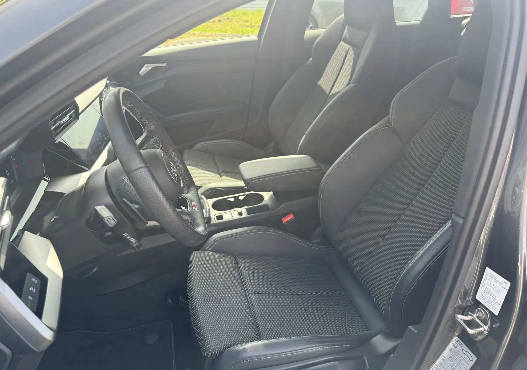Vue intérieure côté conducteur de l’Audi A3 Sportback gris 2023, avec sièges sport S-Line en tissu et cuir noir.