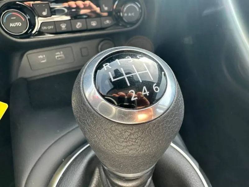 Gros plan sur le levier de vitesses manuel noir et chrome du Nissan Juke blanc nacré 2025 avec commandes climatisation en arrière-plan.