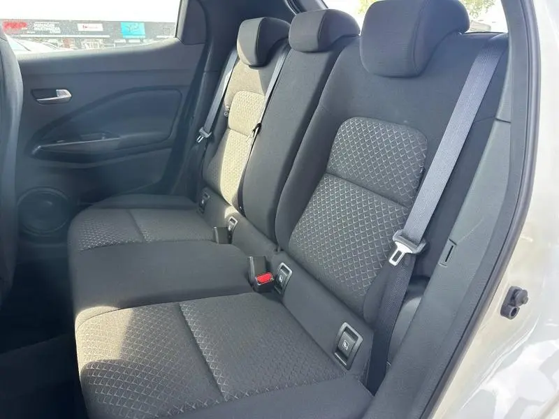 Vue latérale droite de la banquette arrière noire en tissu du Nissan Juke blanc nacré 2025 avec ceintures de sécurité visibles.