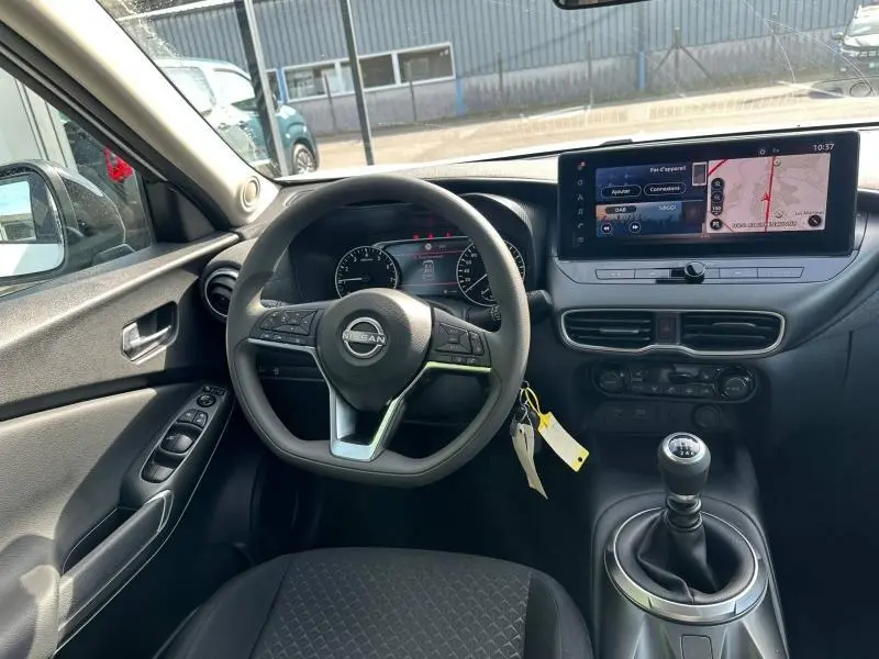 Vue intérieure avant du Nissan Juke 2025 avec volant multifonction, écran tactile et levier de vitesse manuel.