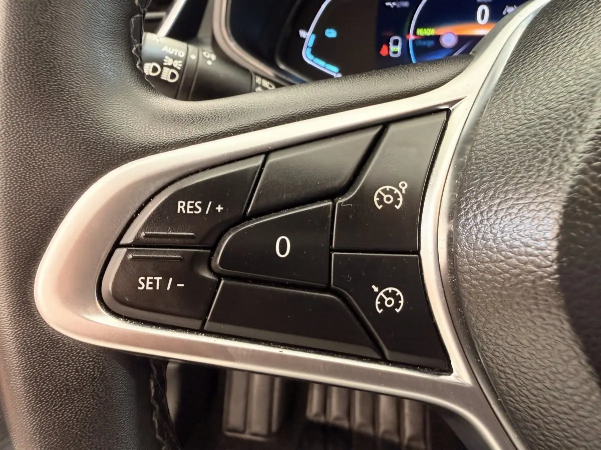 Gros plan sur les commandes du régulateur de vitesse au volant cuir synthétique d'une Renault Clio blanche hybride 2022.
