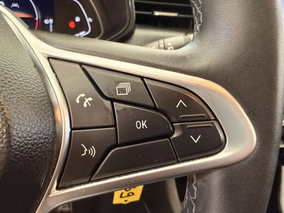 Gros plan sur les commandes multifonctions noires du volant cuir synthétique de la Renault Clio Business E-Tech hybride 2022.