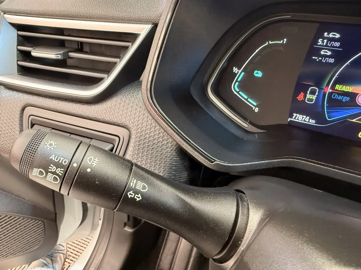Gros plan sur la commande des phares et clignotants à gauche du tableau de bord numérique d’une Renault Clio blanche hybride.