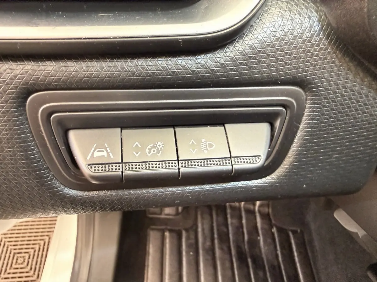 Gros plan sur les boutons de réglage d'assistance à la conduite dans une Renault Clio Business E-Tech hybride blanche.