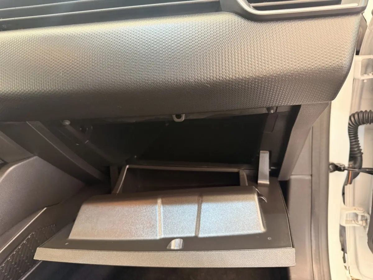 Gros plan sur la boîte à gants ouverte côté passager d’une Renault Clio Business E-Tech blanche, intérieur noir.