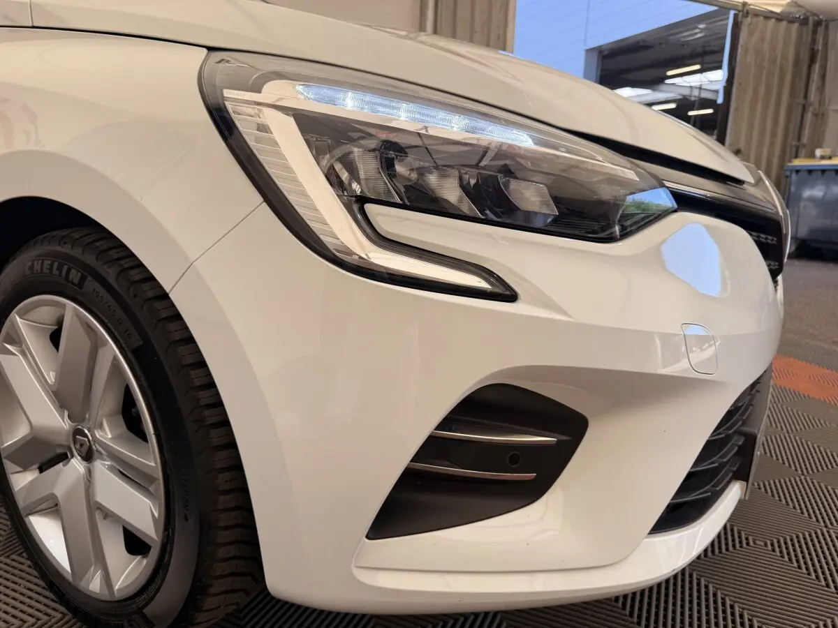 Gros plan sur l'avant droit blanc d'une Renault Clio Business E-Tech hybride 2022, mettant en valeur le phare LED et la jante.